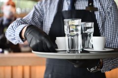 waiter in a medical protective mask serves  the coffee in restaurant durin coronavirus pandemic representing new normal concept