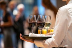 Germany: Female waitress offers red and white wine on a tray.